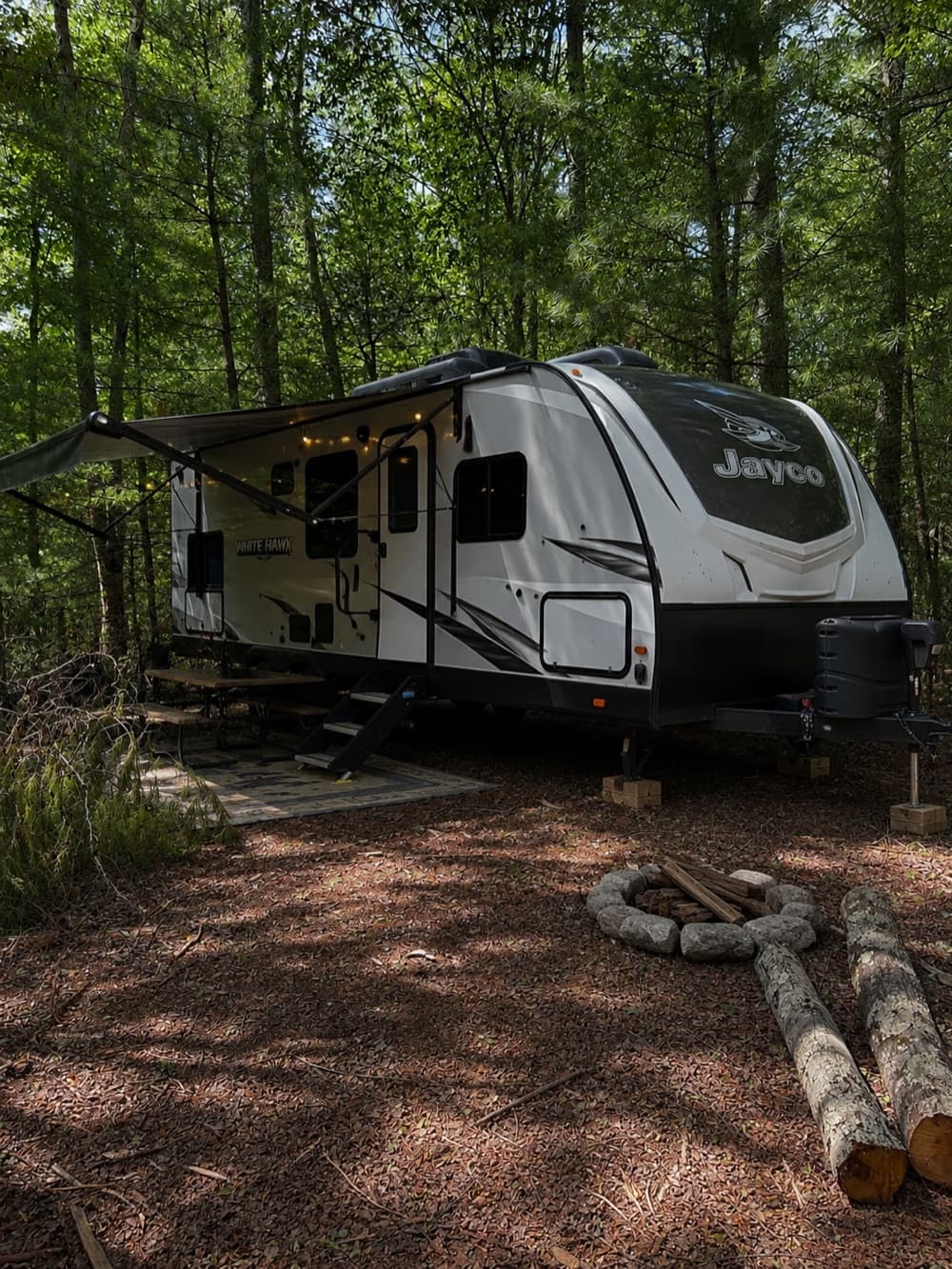 RV parked at a wooded campsite with a fire ring